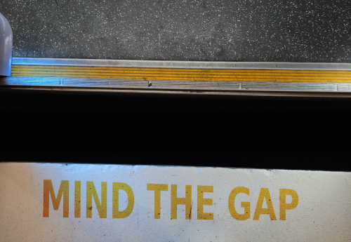 A down angle shot into a platform gap. A warning on the floor reads 'mind the gap'.